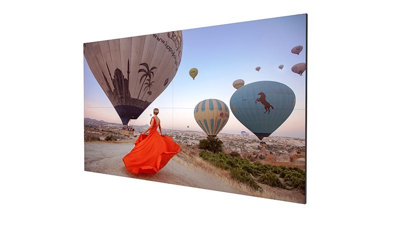 A woman in an orange dress is standing in front of hot air balloons.