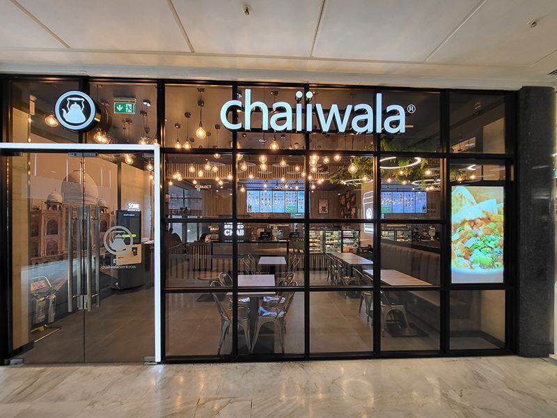 The front of a restaurant called chaiwala with tables and chairs.