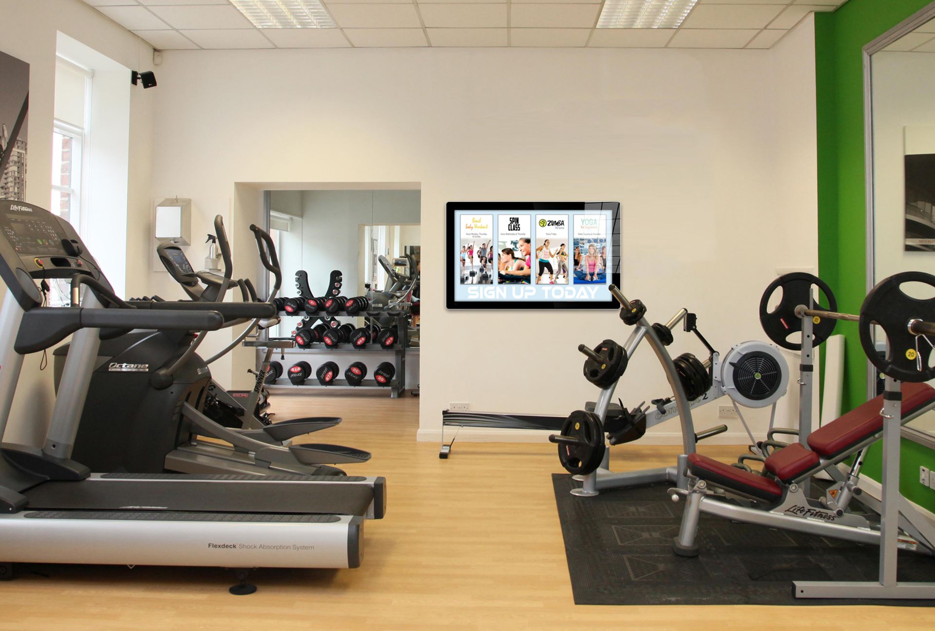 A gym with treadmills , dumbbells , and a flat screen tv on the wall.