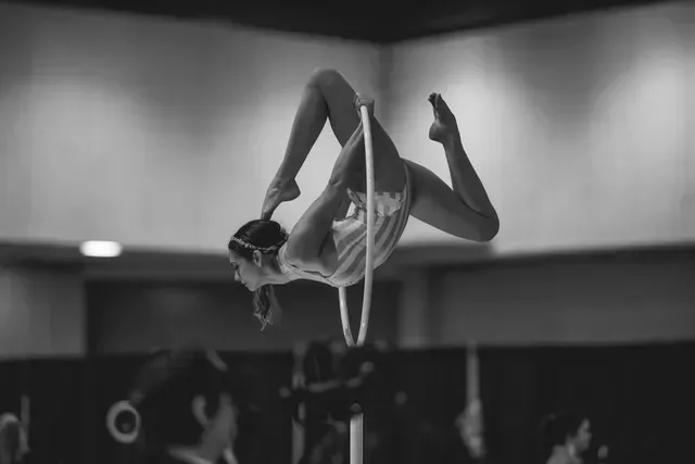 A gymnast in a leotard performs a backbend pose inside an aerial hoop suspended in a gym.