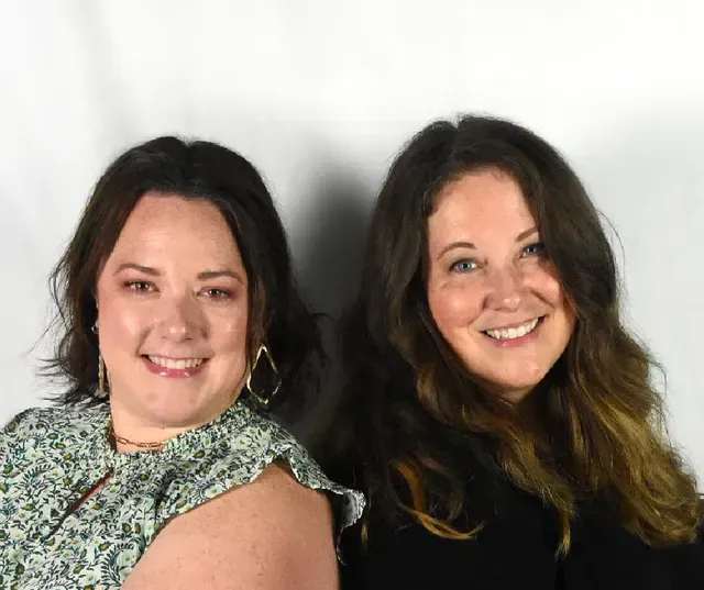 Two people posing side-by-side against a plain white background, both smiling at the camera.