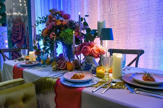 An elegant dining table set with floral arrangements, candles, fruits, and plates of pasta in a softly lit room.