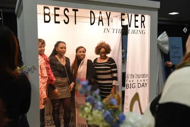 Four people pose for a photo inside a booth labeled 