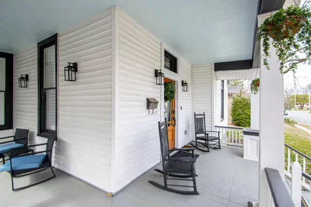 A white porch with light blue ceiling, gray floor, black rocking chairs, and wall-mounted lantern lighting.