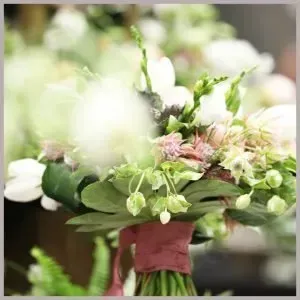 A wedding bouquet of white and blush flowers and greenery, tied together with a dusty rose ribbon.