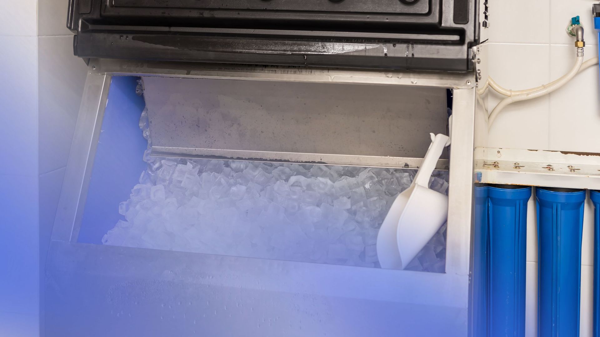 A machine is making ice in a kitchen with a scoop in it.