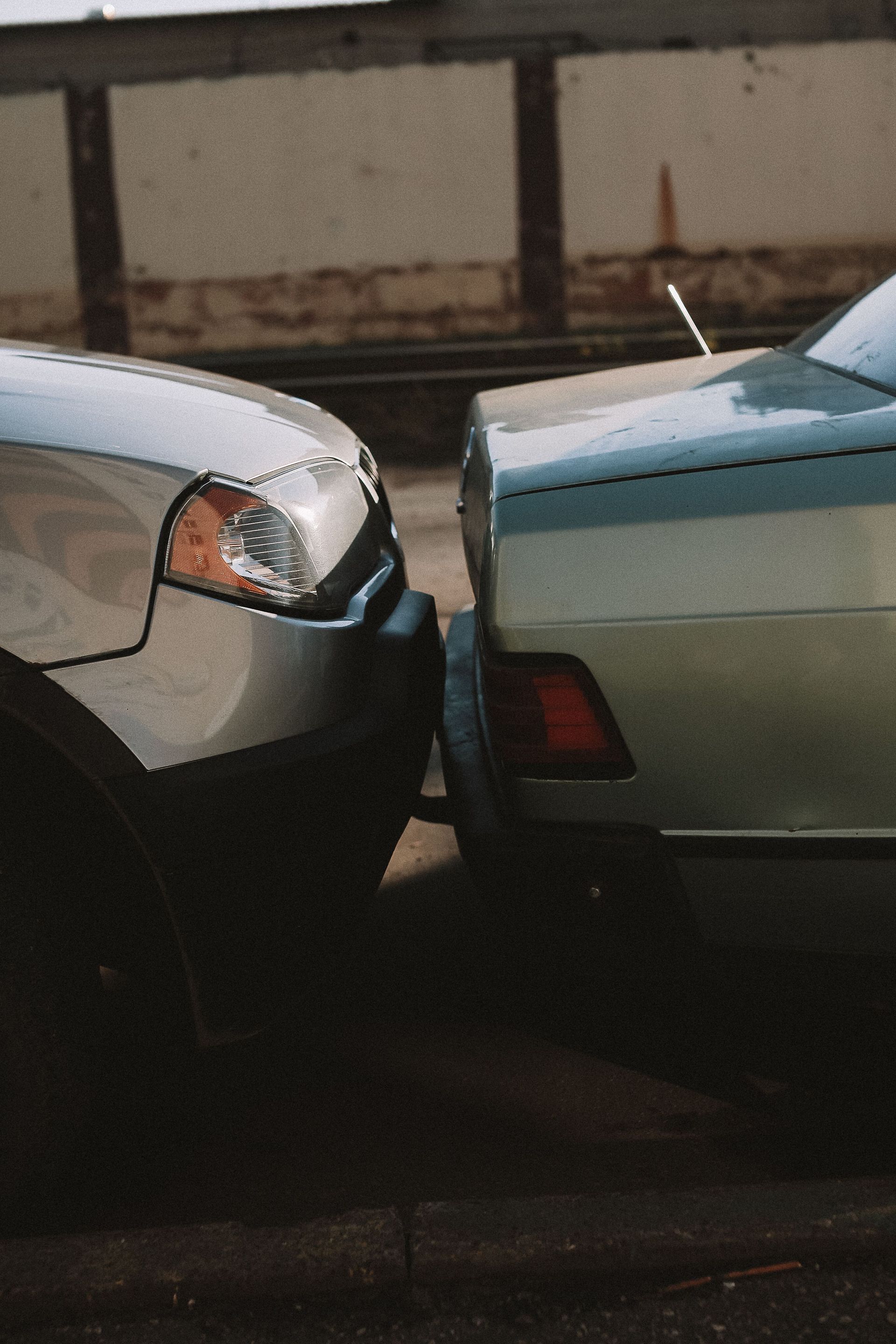 Two parked cars bumper-to-bumper in a tight space, one silver and one green.