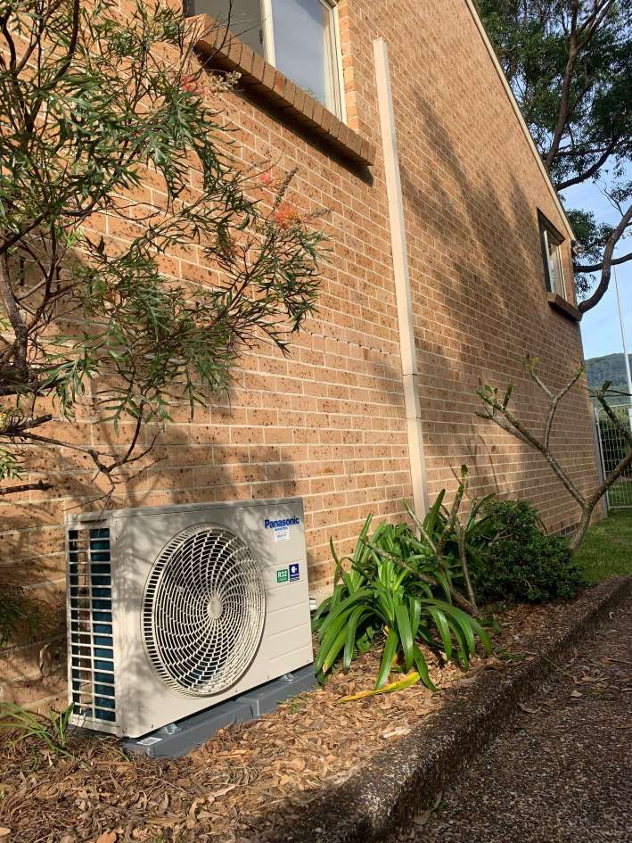 A Large Air Conditioner Is Sitting On The Side Of A Brick Building — Rapidcool Air Conditioning & Electrical In Dapto, NSW