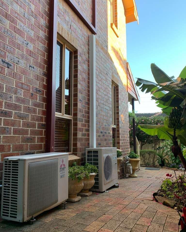 Two Air Conditioners Are Sitting On The Side Of A Brick Building — Rapidcool Air Conditioning & Electrical In Dapto, NSW