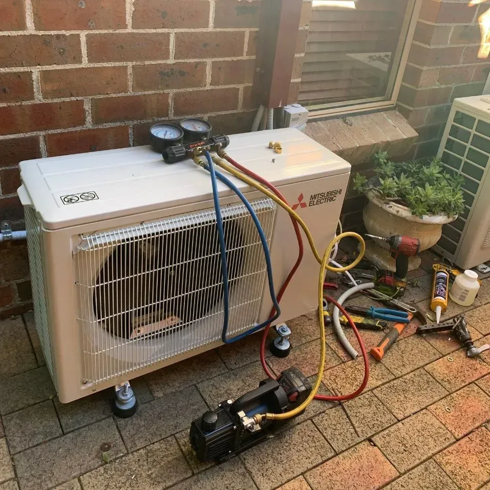 A Mitsubishi Air Conditioner Is Being Repaired On A Brick Sidewalk — Rapidcool Air Conditioning & Electrical In Dapto, NSW