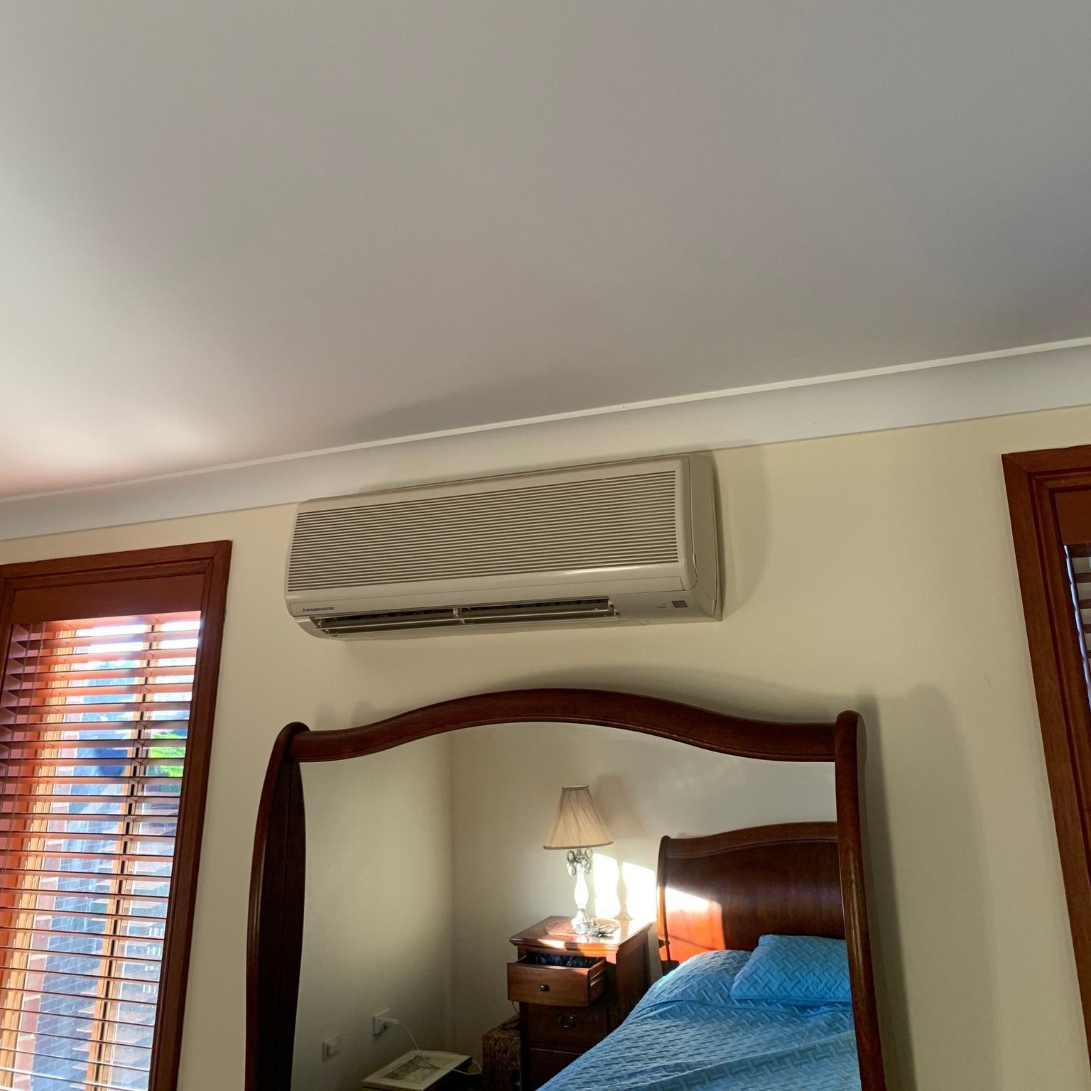 A Bedroom With A Bed, Mirror, Air Conditioner, And Window Blinds — Rapidcool Air Conditioning & Electrical In Dapto, NSW
