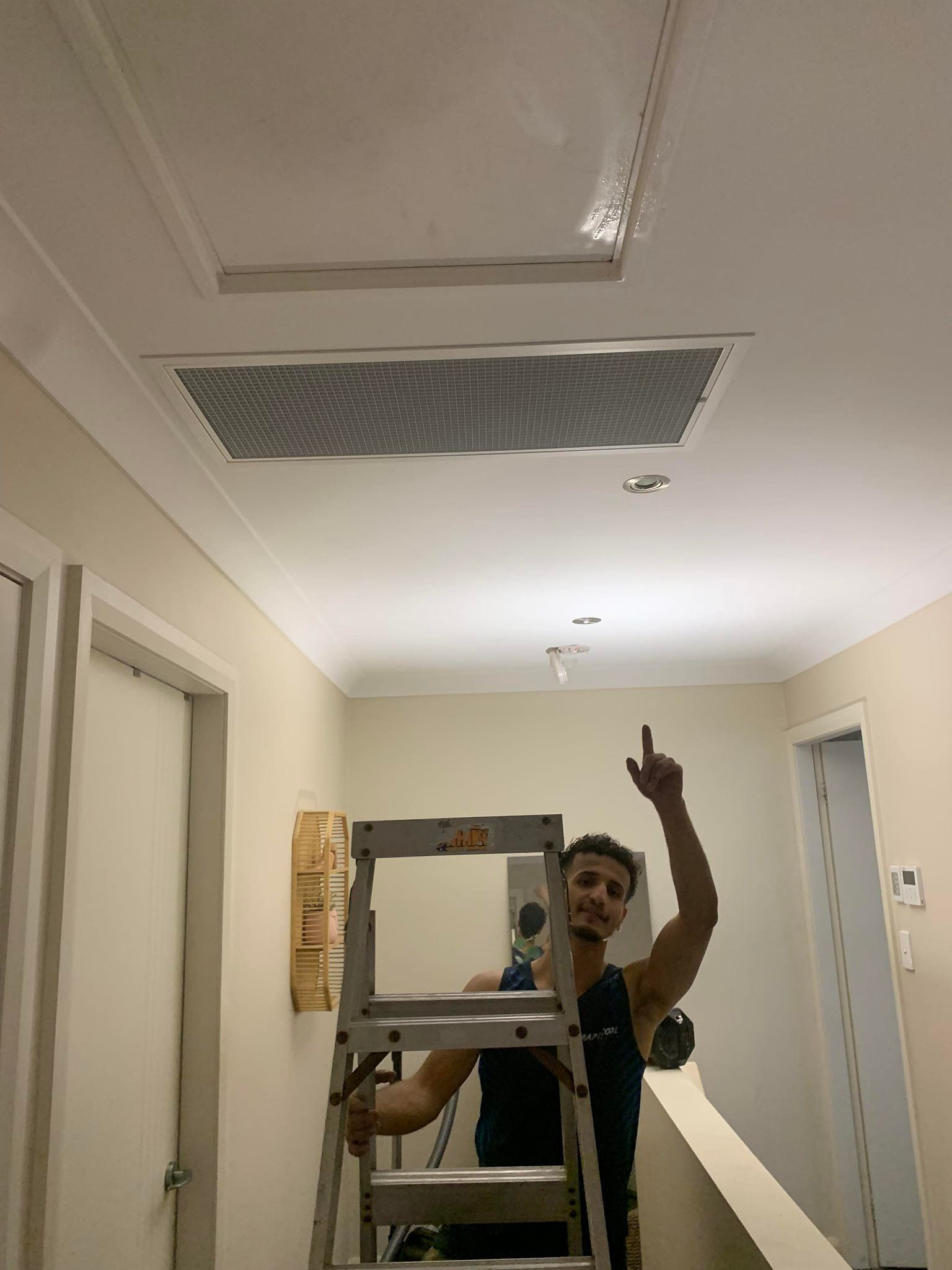 A Man Is Pointing To A Ducted Air Conditioner — Rapidcool Air Conditioning & Electrical In Dapto, NSW