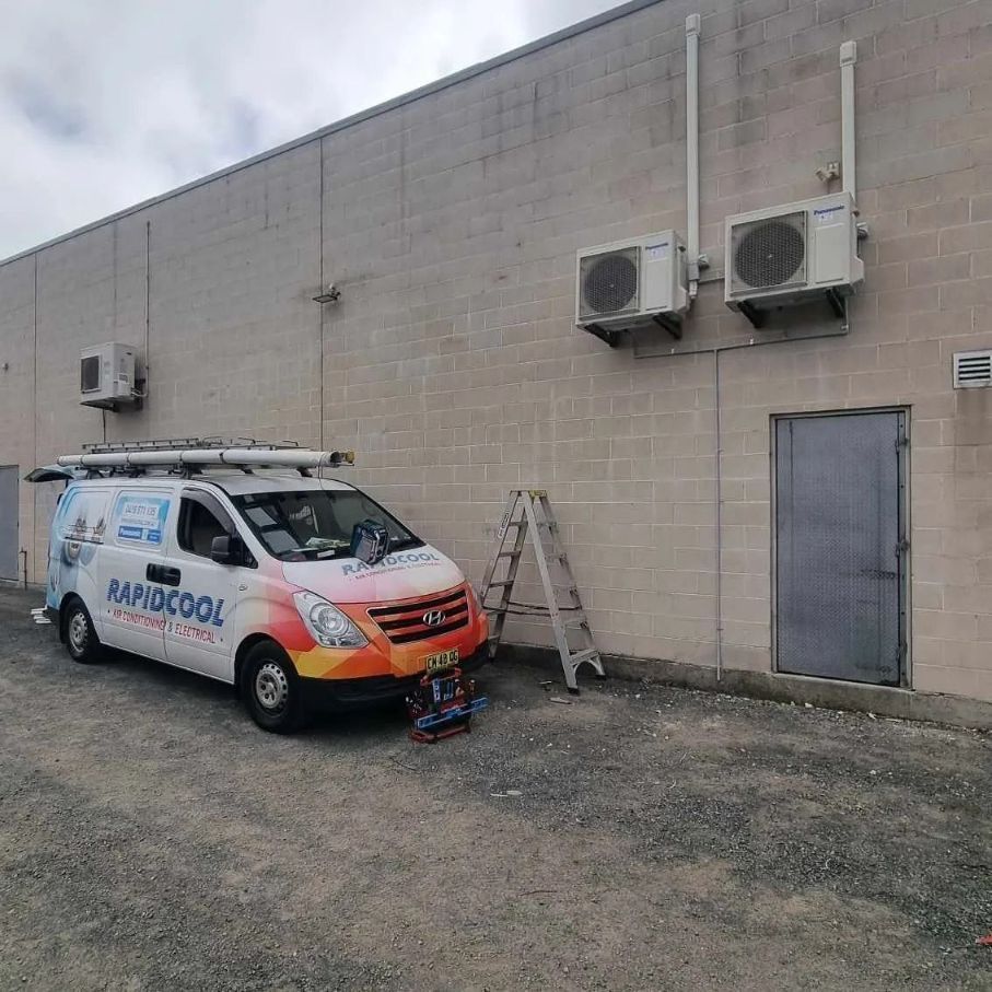 A White Van Is Parked In Front Of A Brick Building — Rapidcool Air Conditioning & Electrical In Dapto, NSW