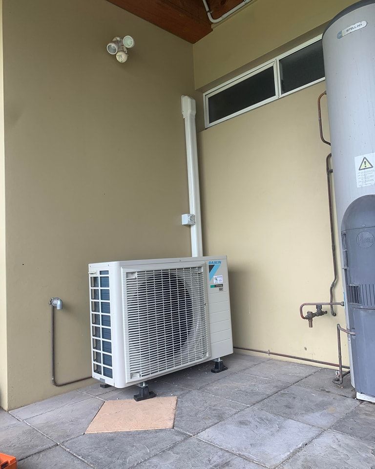 A White Air Conditioner Is Sitting Next To A Water Heater — Rapidcool Air Conditioning & Electrical In Albion Park, NSW