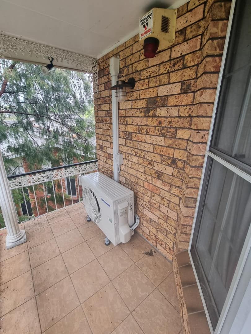 A Brick Wall With an Air Conditioning Unit — Rapidcool Air Conditioning & Electrical In Wollongong, NSW