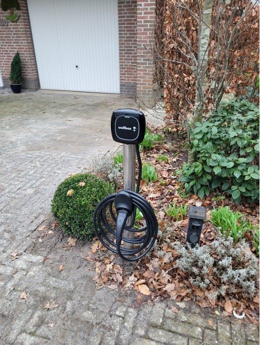 Een laadstation voor een elektrische auto staat aan de zijkant van een oprit.