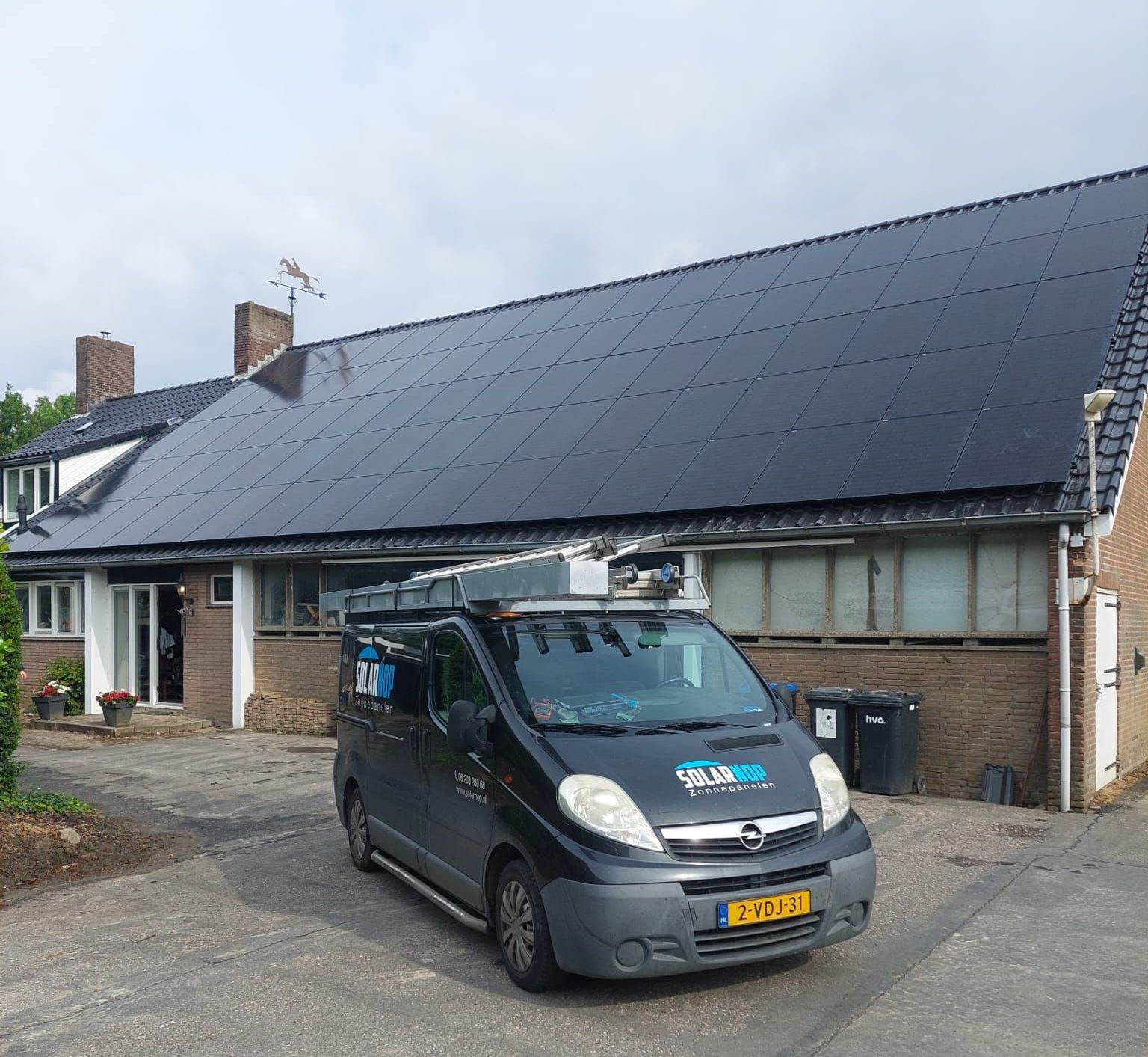 Een busje geparkeerd voor een huis met zonnepanelen op het dak