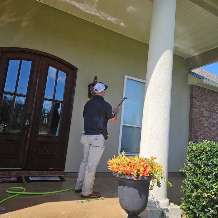 Man washing a window outside a building. He is near a column with flowers and a door.