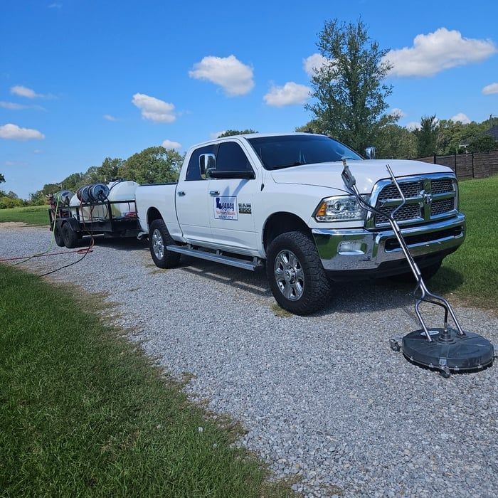 White pickup truck with trailer, pressure washer on gravel driveway, sunny day.
