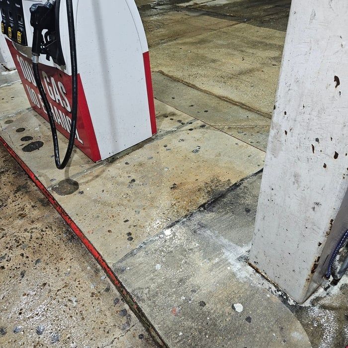 Gas pump island with gray concrete and a red border. The area has concrete spillage and stains.