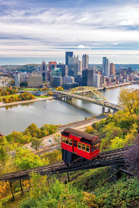 A red train is going down a hill with a city in the background.