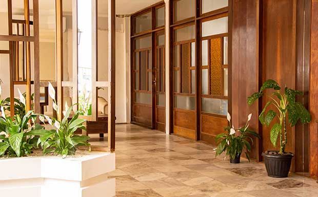 Corredor com portas de madeira, piso estampado e vasos de plantas.