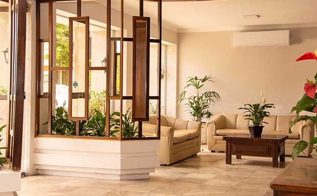 Sala de estar com divisória de madeira, sofás bege, plantas e mesa de centro.