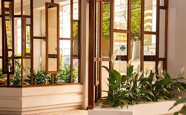 Divisória de madeira com jardineiras embutidas repletas de plantas verdes; muita luz natural.