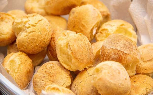 Pãezinhos de queijo dourados e assados em uma cesta.