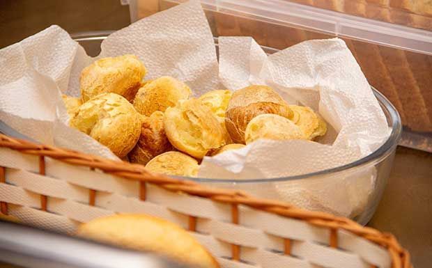 Cesta de pão de queijo dourado, forrada com papel toalha, em uma tigela de vidro.