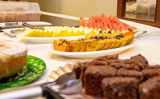 Buffet de café da manhã com melão fatiado, mamão papaia, melancia e brownies de chocolate.