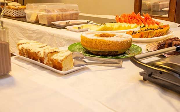 Buffet de café da manhã com bolos, frutas e máquina de waffles.