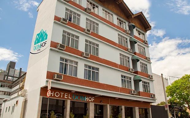 Exterior do hotel com fachada azul clara, detalhes em vermelho e o nome