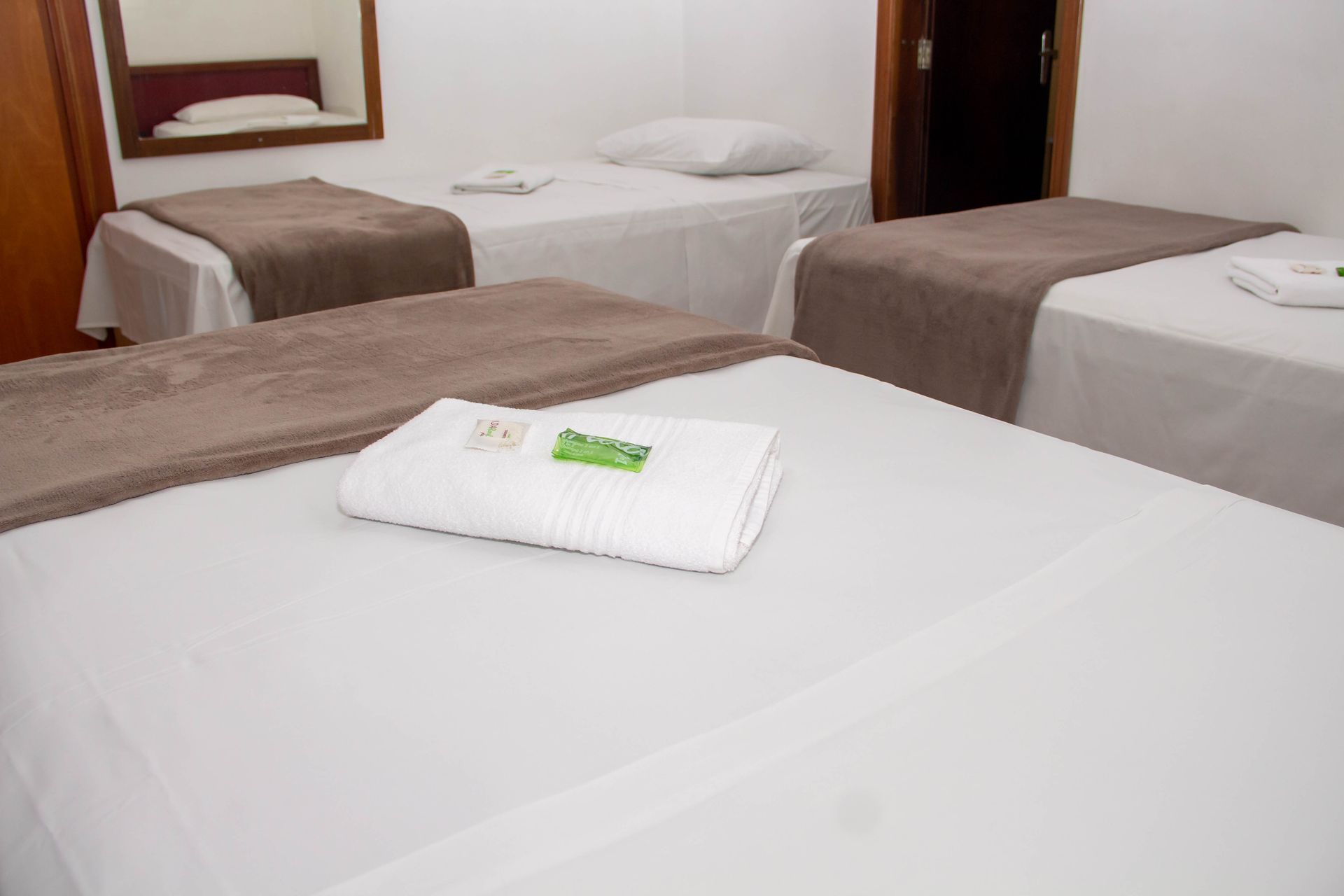 Um quarto com três camas de solteiro, lençóis brancos, mantas marrons e um espelho.