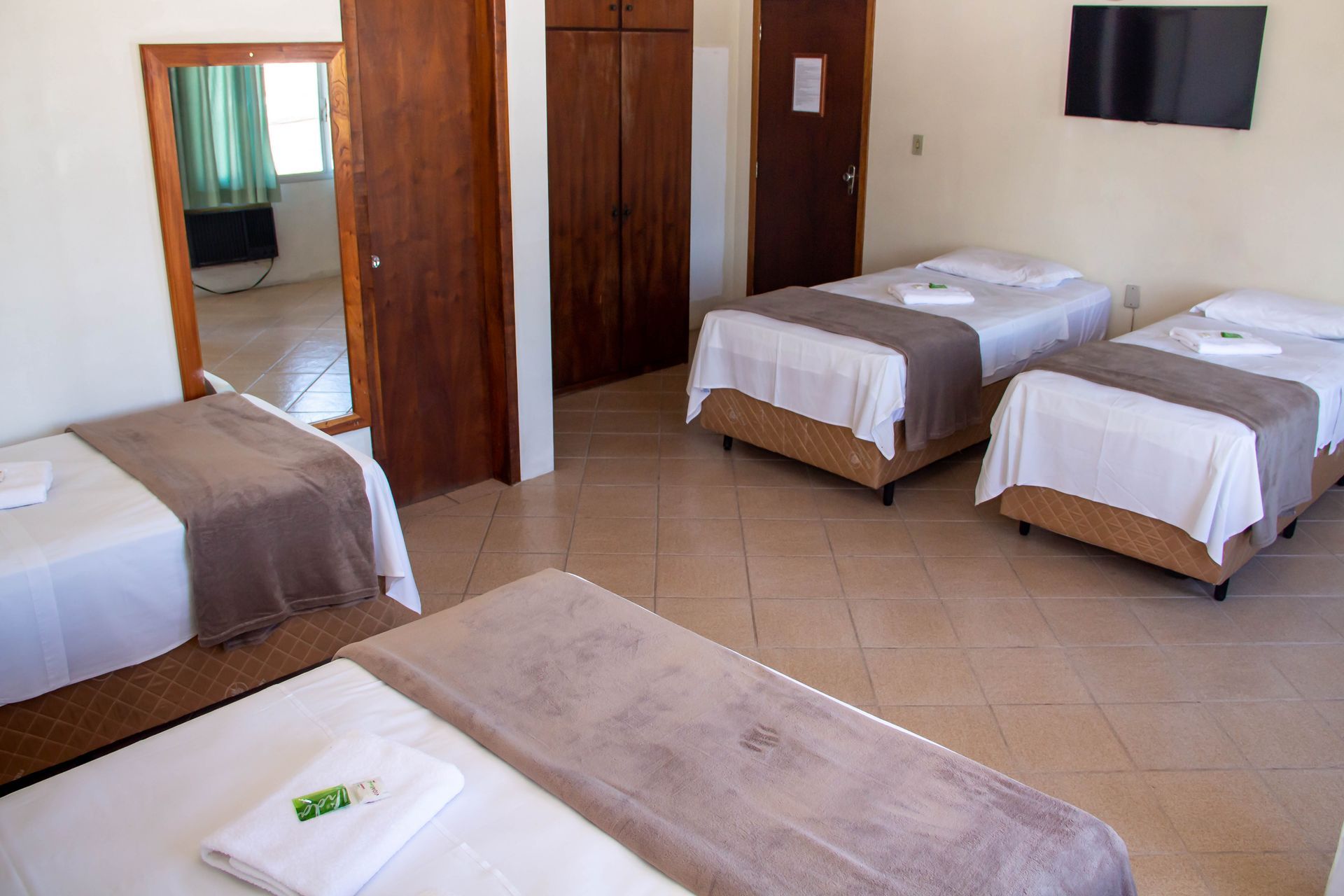 Quarto de hotel com quatro camas, um espelho e uma TV fixada na parede.