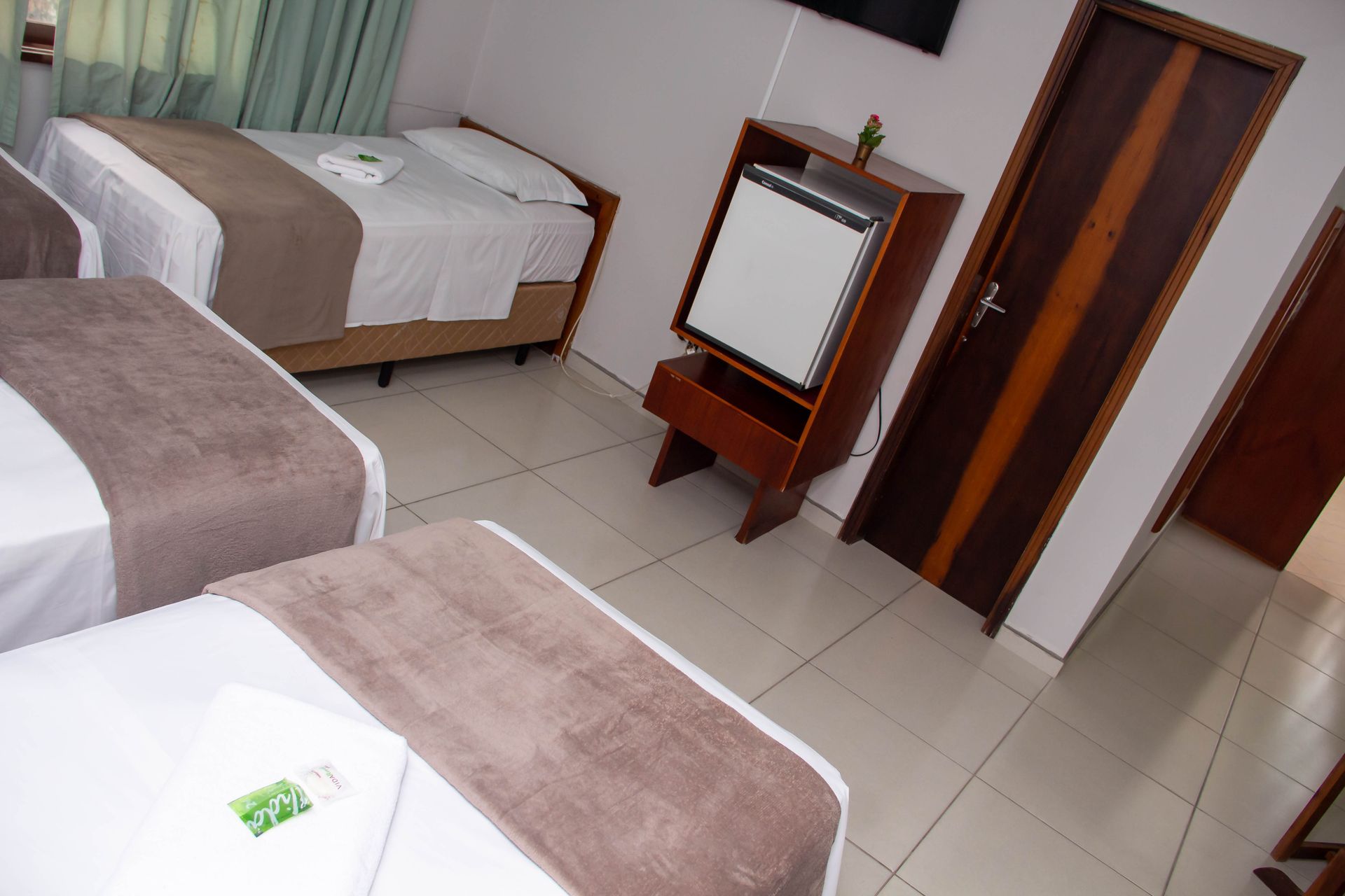 Quarto de hotel com três camas, frigobar e porta fechada.