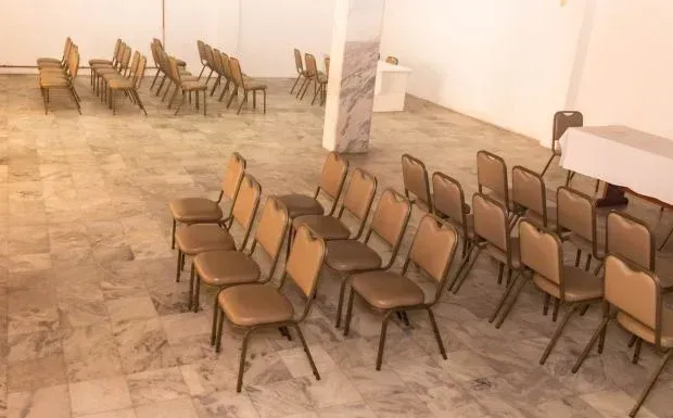 Sala vazia com fileiras de cadeiras bege dispostas para um evento. Paredes brancas e piso de mármore.