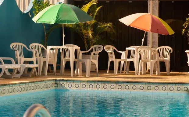 Cena à beira da piscina com mesas, cadeiras e guarda-sóis.