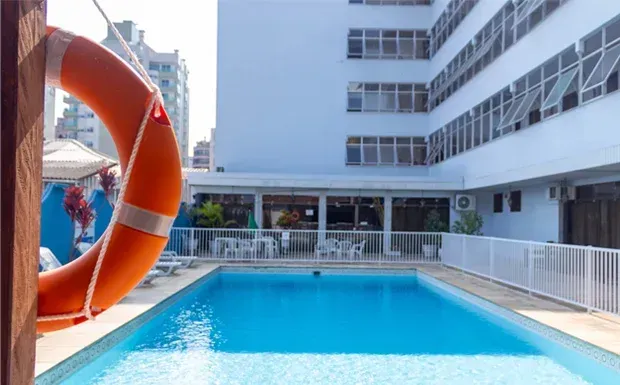 Uma boia salva-vidas laranja está pendurada perto de uma piscina, com um hotel ao fundo.