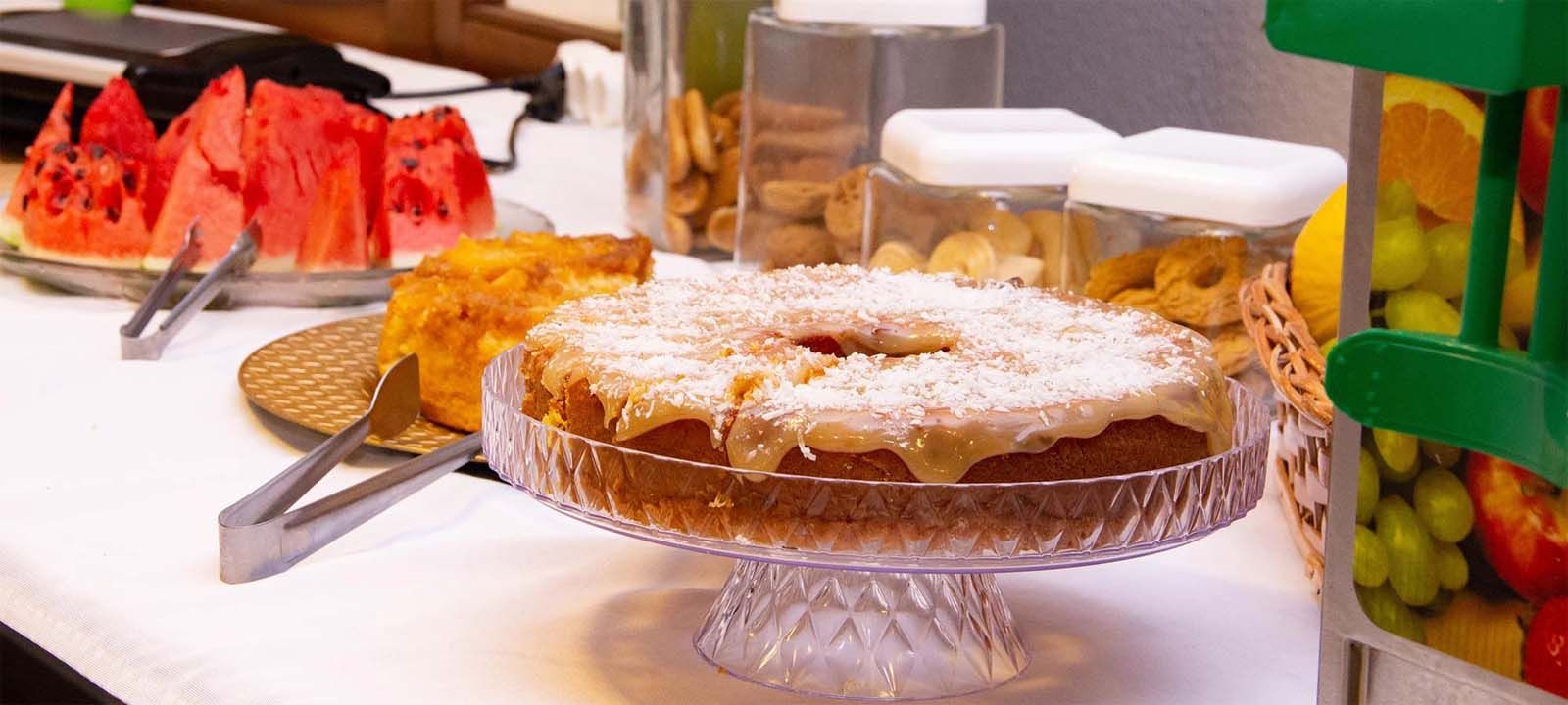 Uma mesa com uma variedade de alimentos: melancia, bolo e biscoitos em potes.