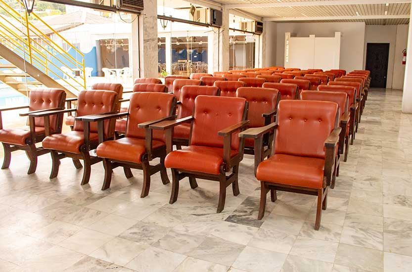 Fileiras de cadeiras de couro laranja em um hall com piso e janelas de mármore.