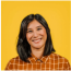 A woman in a plaid shirt is smiling in front of a yellow background.