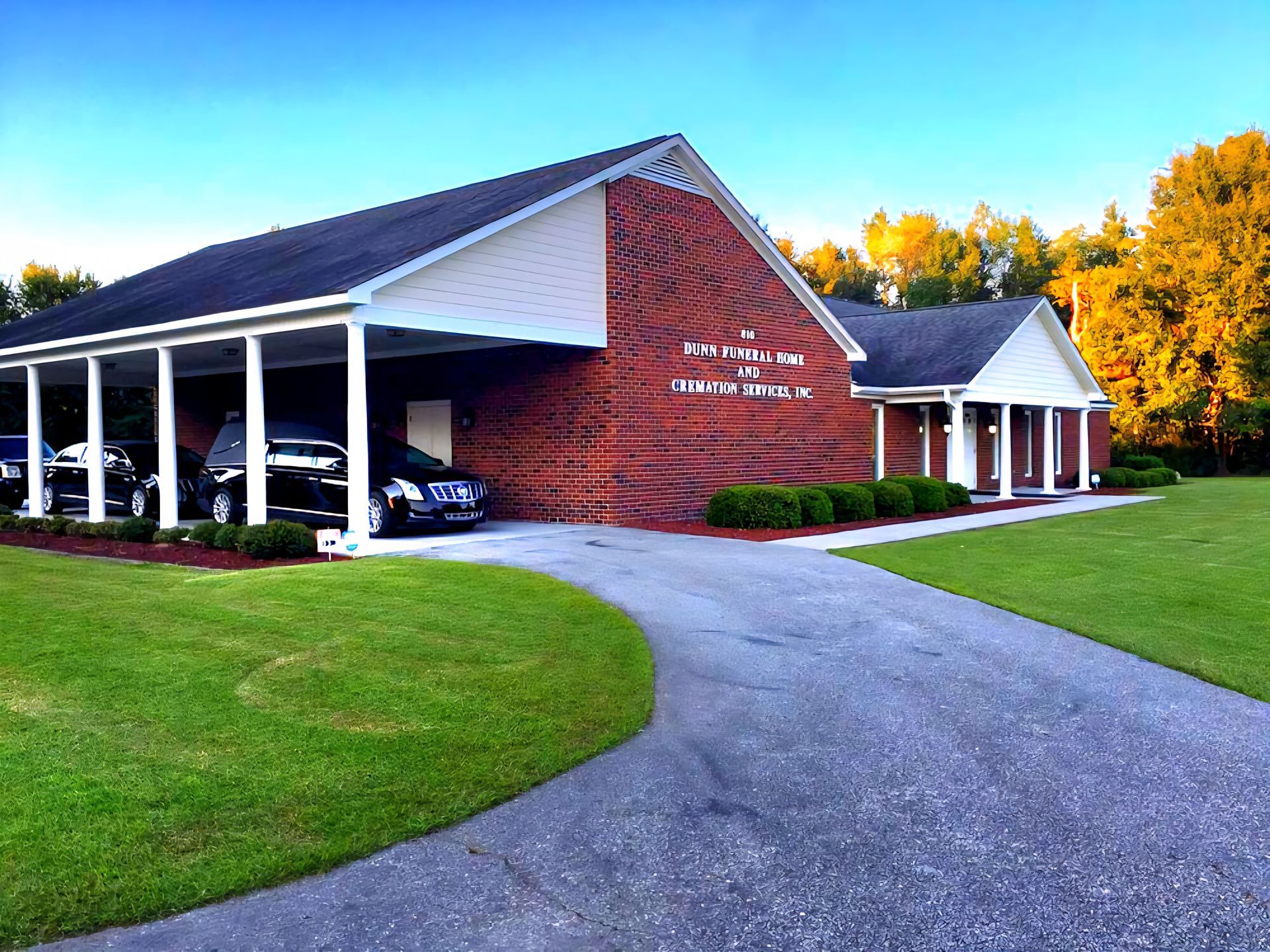 Funeral home, brick building with covered carports, green lawn, asphalt driveway.