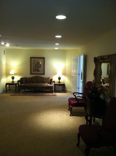 Spacious, carpeted room with sofa, lamps, chairs, and large mirror; soft lighting.