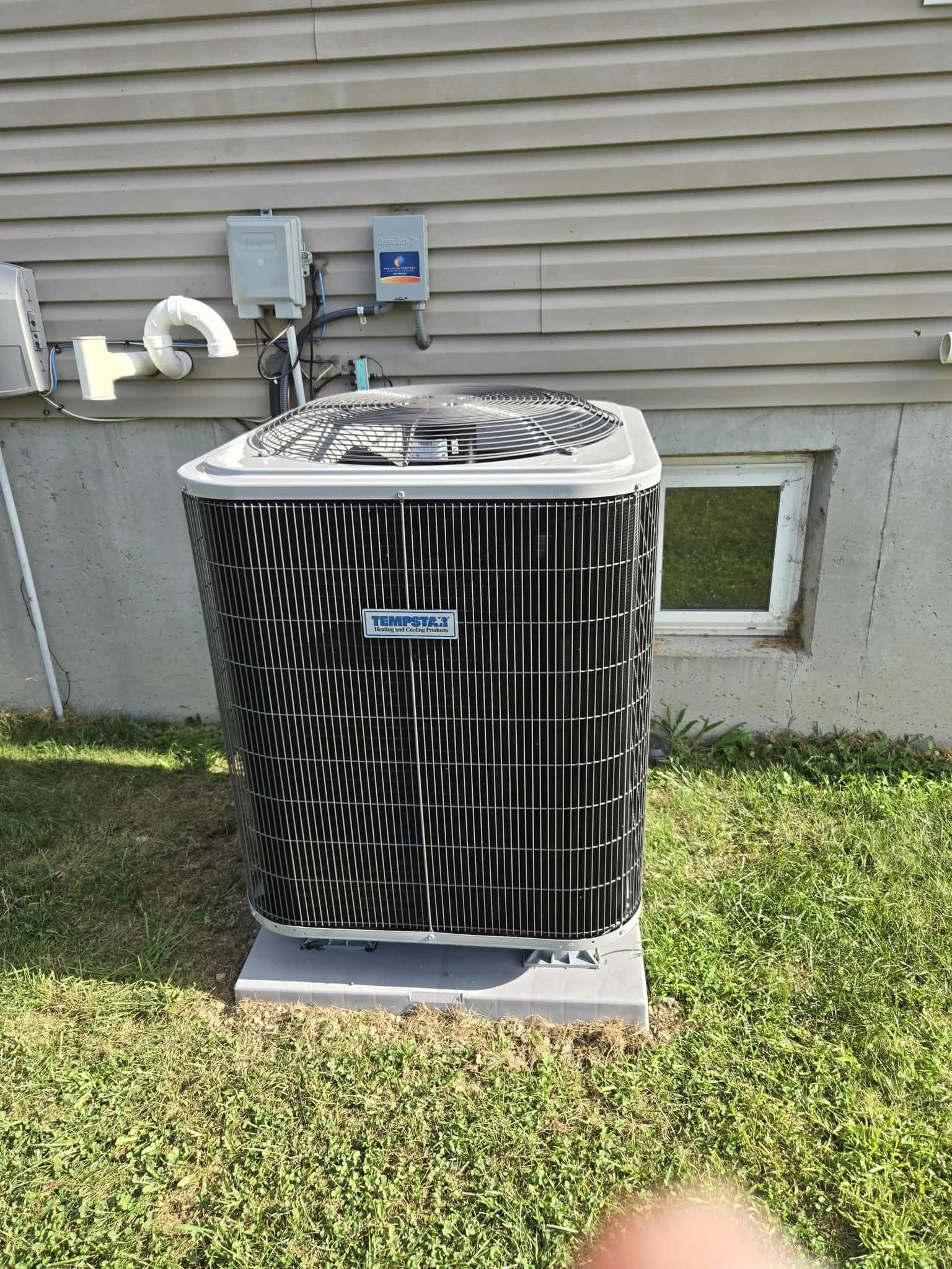 An air conditioning unit outside a building with gray siding, sitting on a concrete pad.