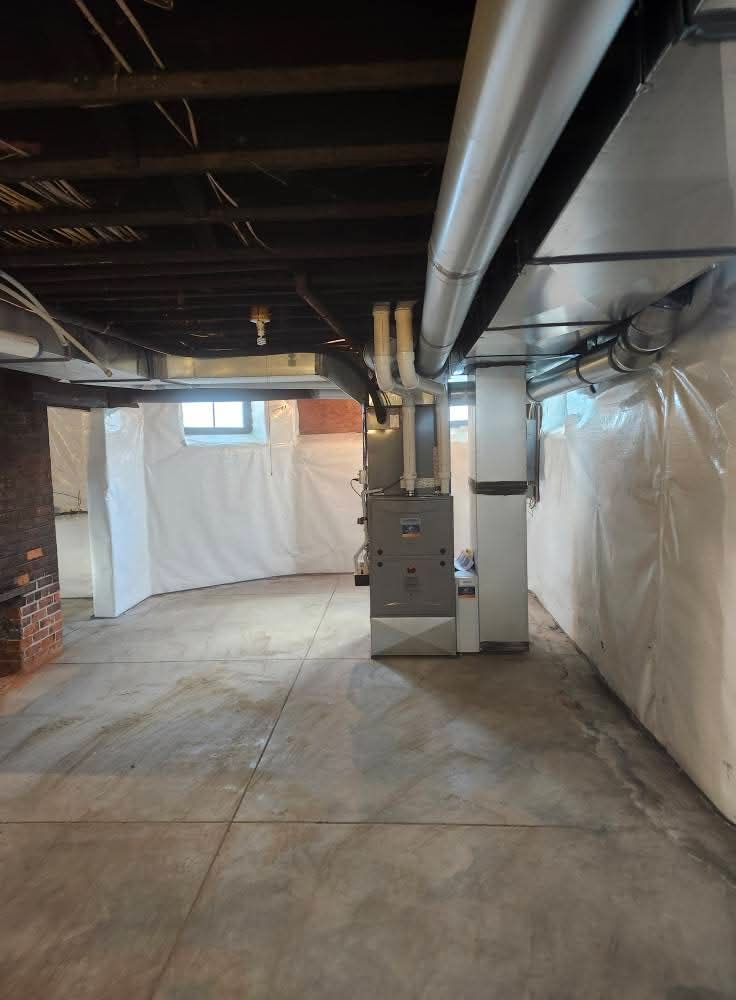 Basement with concrete floor, furnace, ductwork, and white plastic-covered walls.