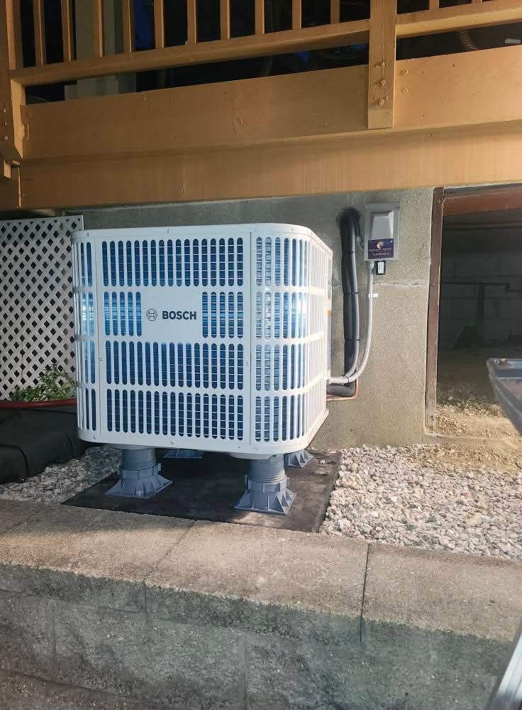 Bosch air conditioner on a gray concrete base, outside beneath a wooden deck.