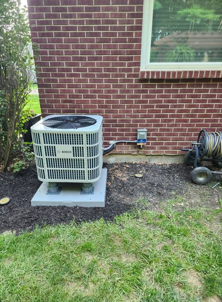 Air conditioner unit on a concrete pad next to a brick wall.