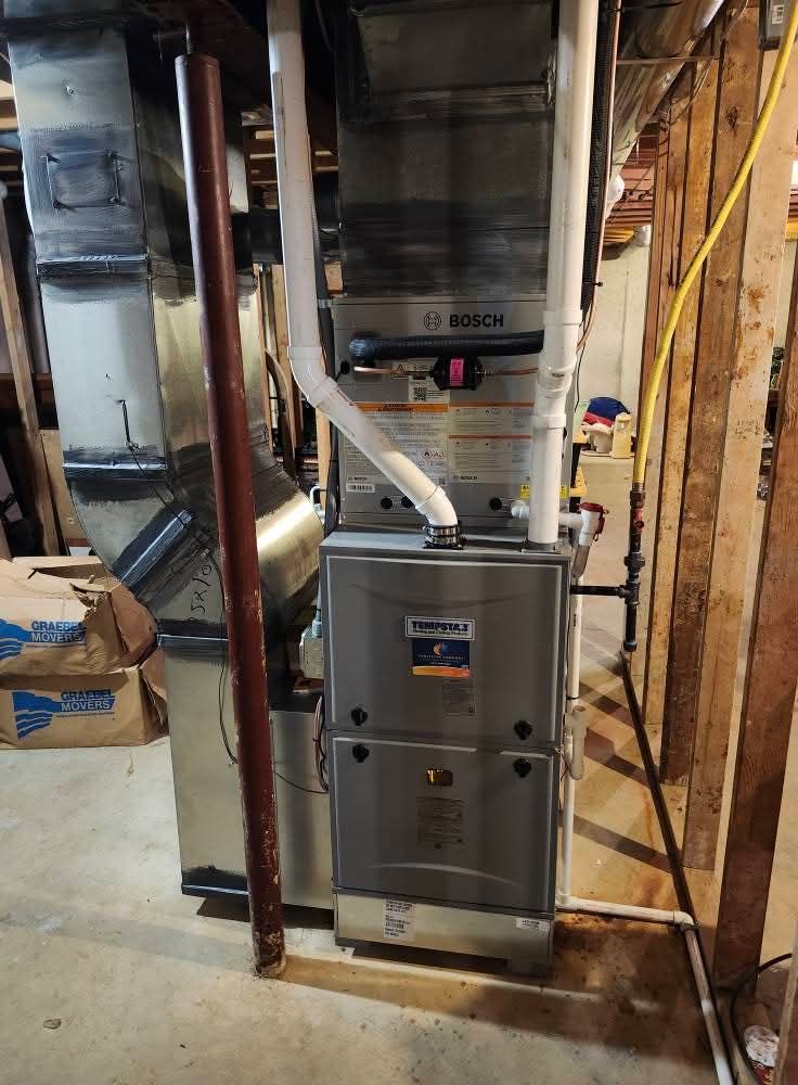 Furnace in basement with ductwork and pipes, mounted between wooden studs.