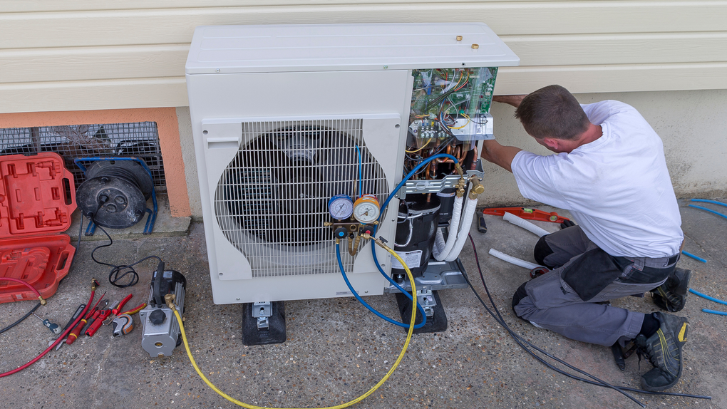HVAC technician working on an outdoor air conditioning unit next to a house.